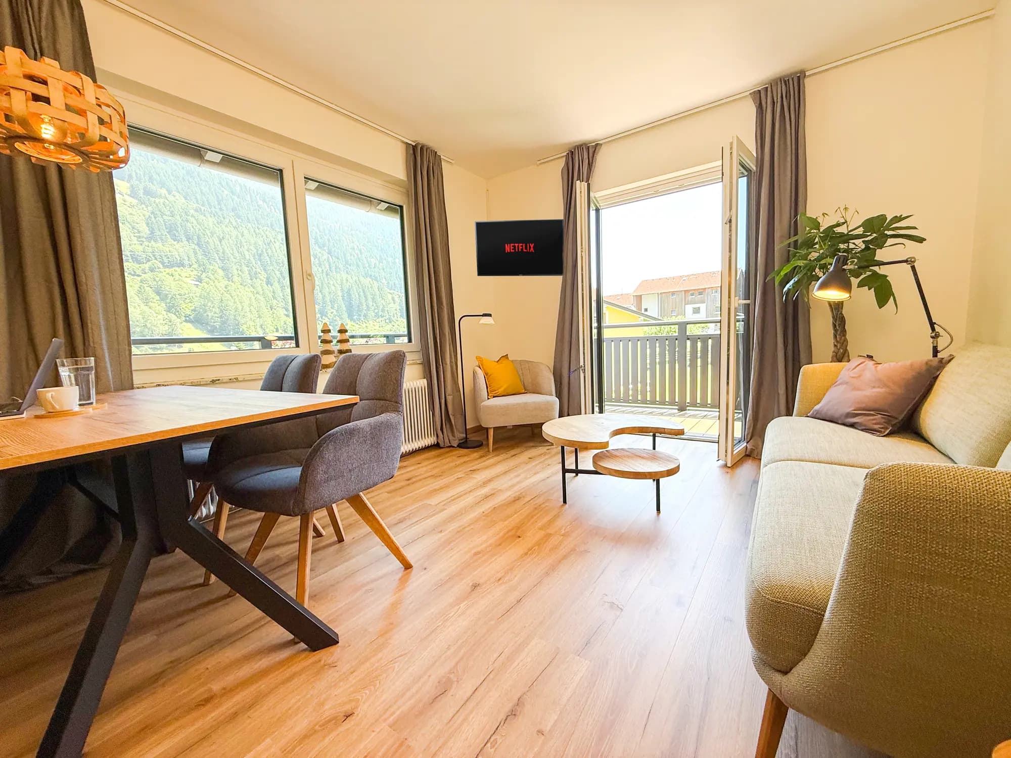 Helles Wohnzimmer der Ferienwohnung Steinbock mit Esstisch, Sitzecke und Balkontür
