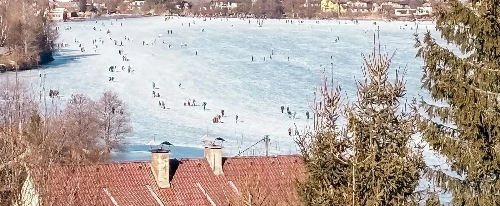 Eisläufer auf dem zugefrorenen Brennsee, im Hintergrund der Ort